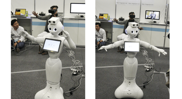 Pepperの後ろでヘッドセットを付けているのがユーザ。ユーザが腕を前に出すとPepperも腕を前に出し、ユーザが頭を左に向けて手を広げるとPepperもその通りの動作をする（PAC2015の会場HUGブースにて）